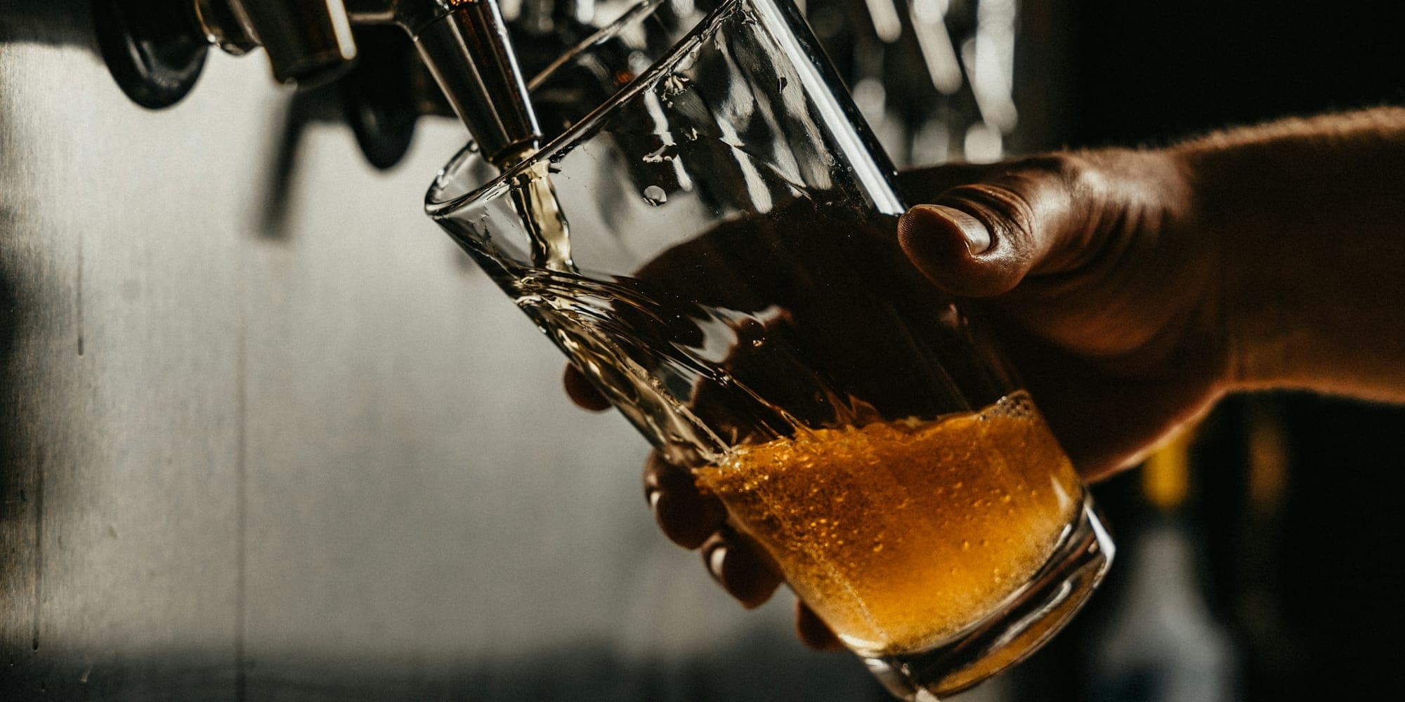 Hand holding a tilted glass under a draft faucet as golden beer pours in