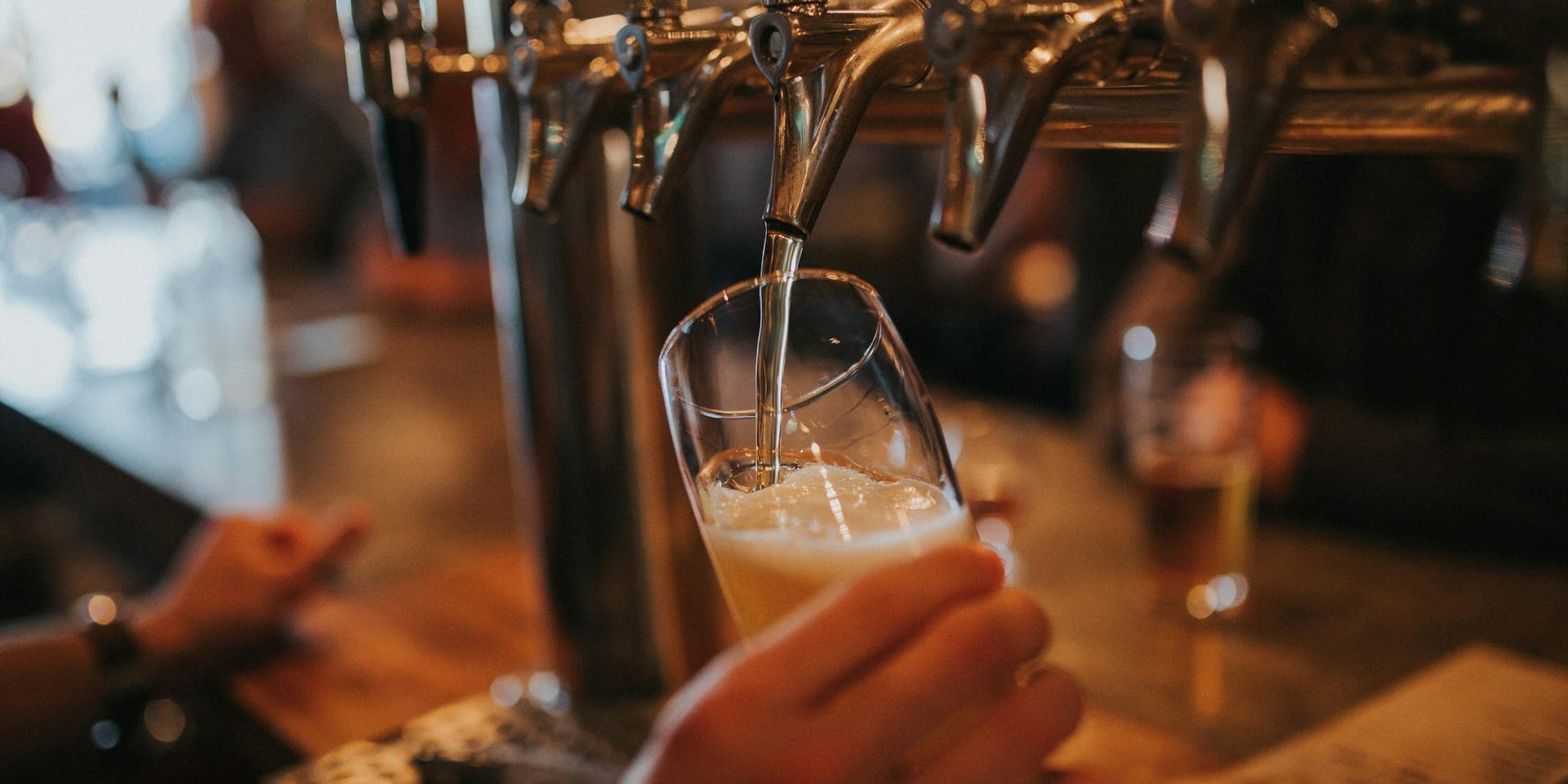 Beer pouring from a draft tower faucet into a glass held at the bar