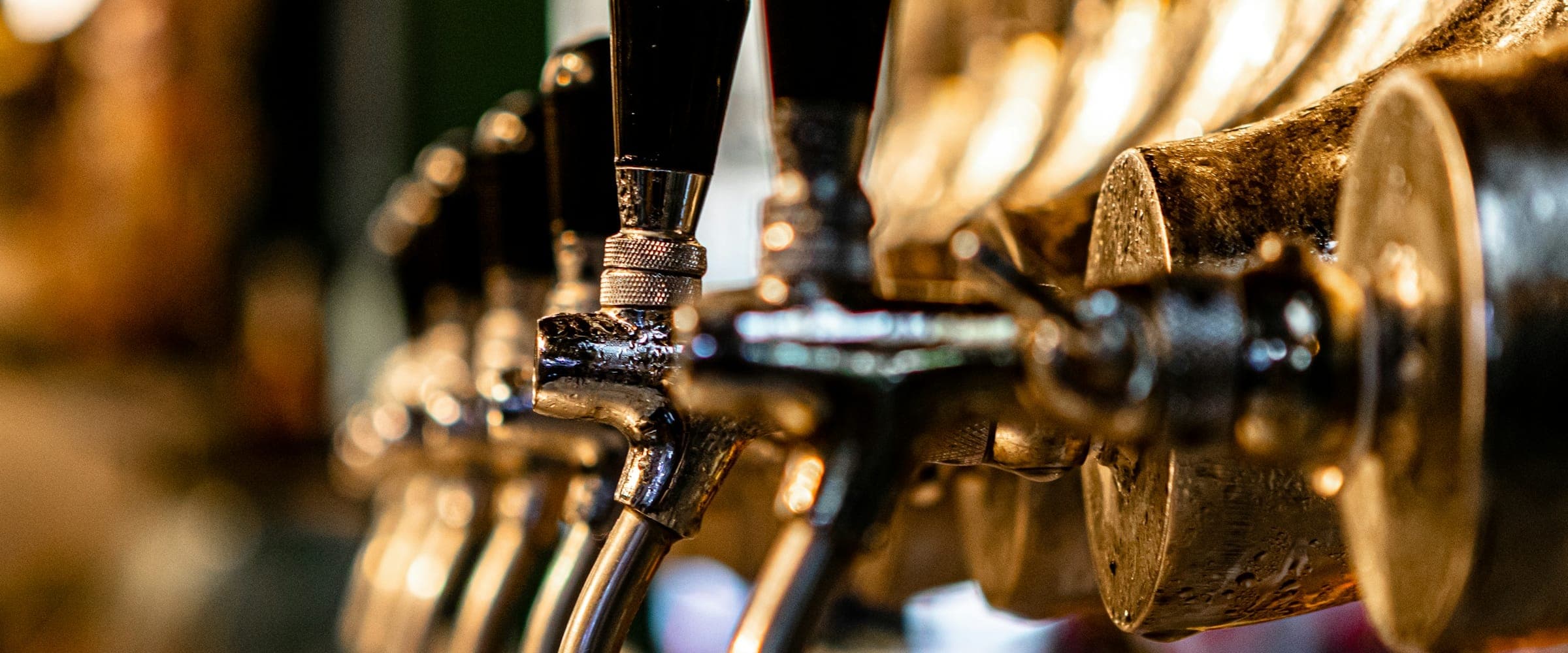Close-up of a row of chrome draft beer faucets with black tap handles